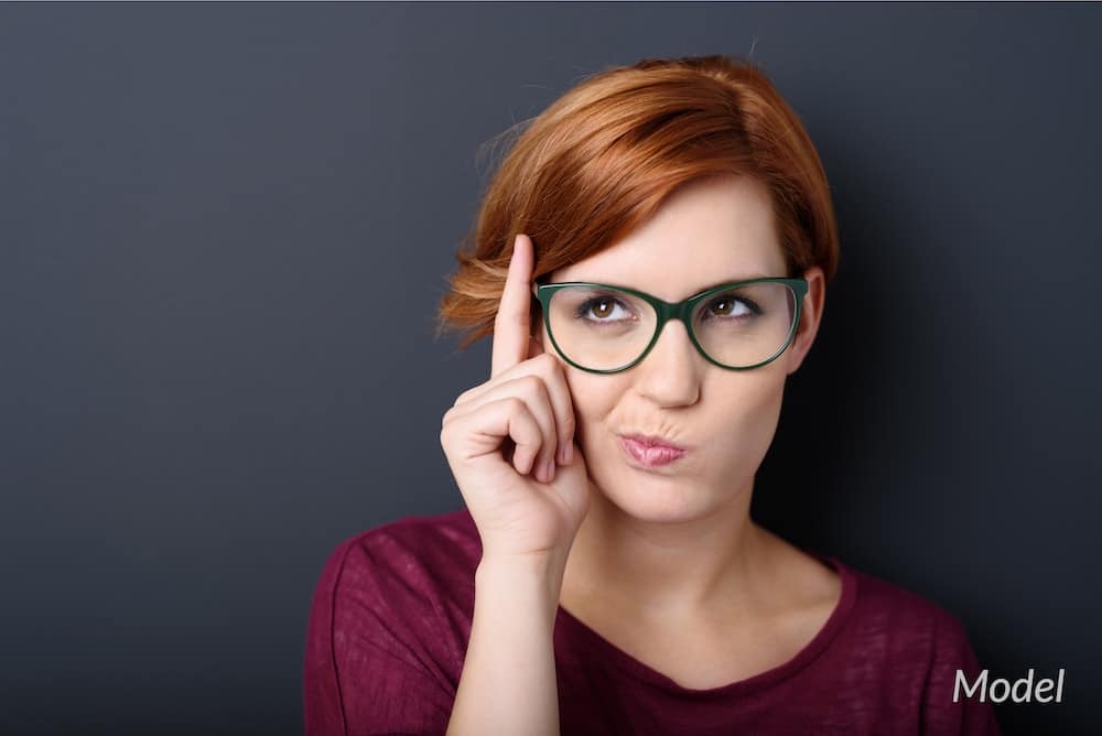 Woman with glasses thinking about her plastic surgery choices