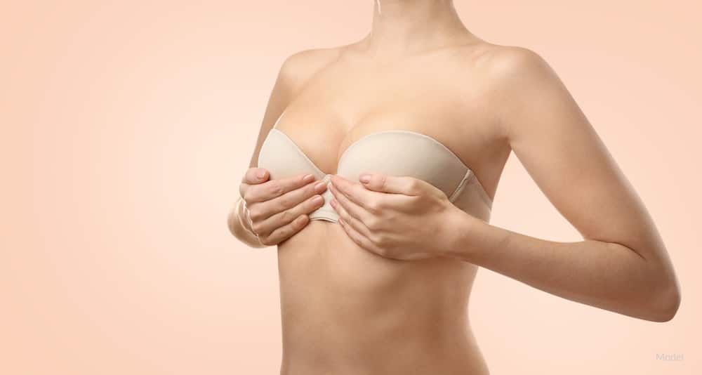 A woman holding her lifted breasts while wearing a bra.