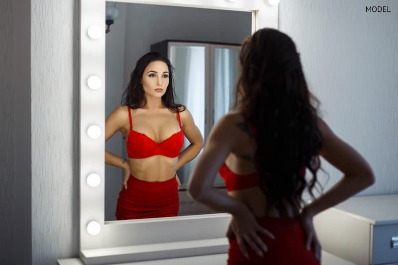 Woman looking at her figure in the mirror, wearing a red bra.