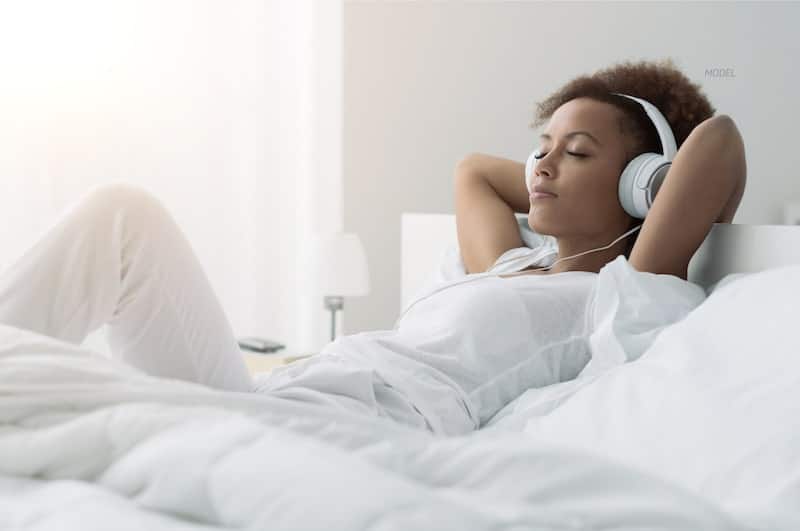 Woman lounging in bed wearing headphones.