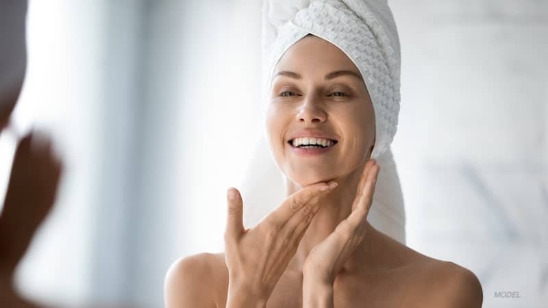 A woman smiles as she cares for her skin.