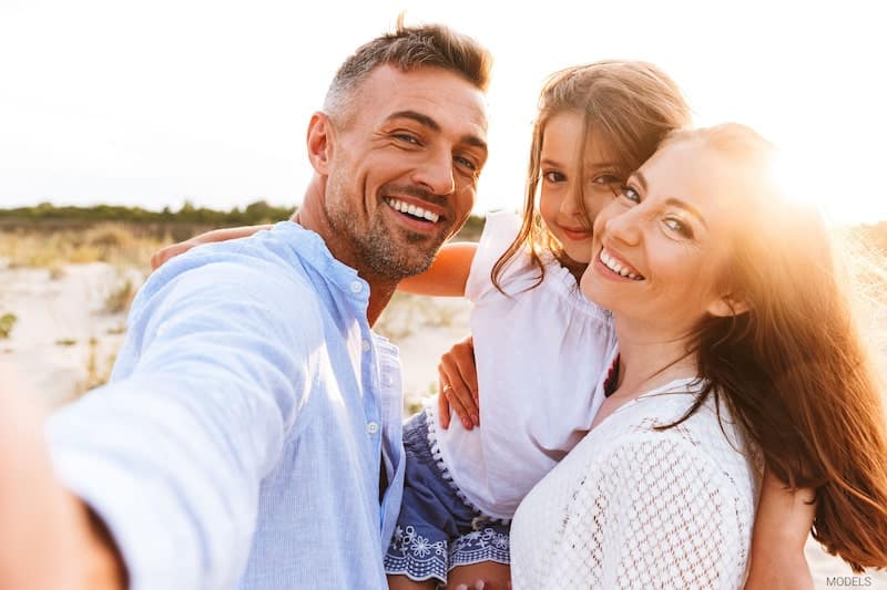 Beautiful mother, father, and daughter at the beach with the sun behind them