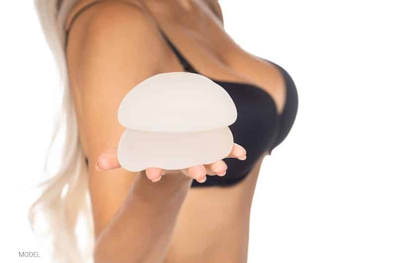Woman holding two breast implants in hand.