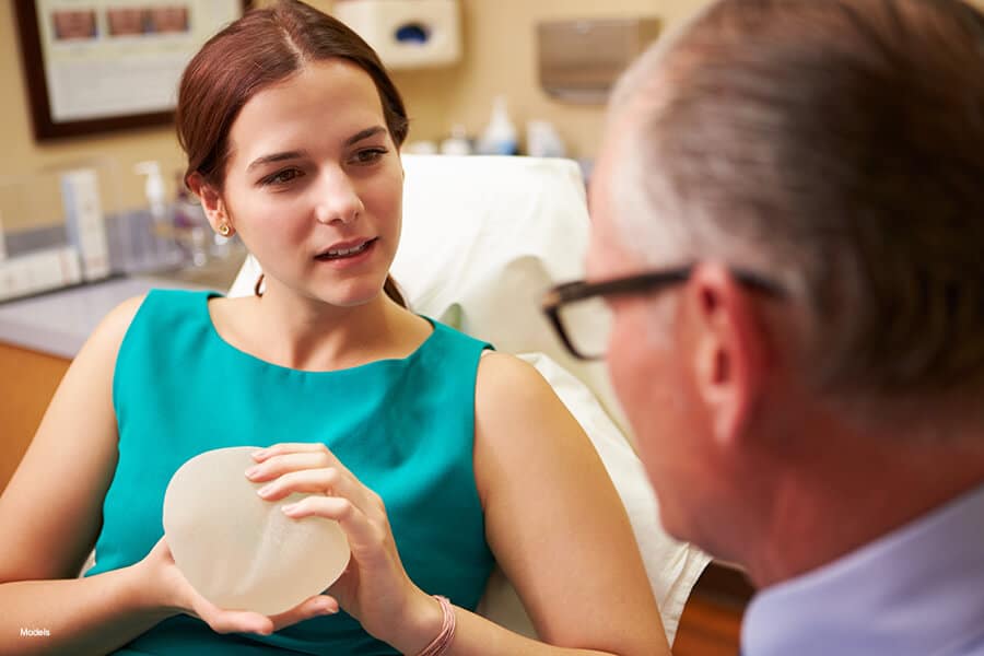 A woman discusses her options with a plastic surgeon while holding a breast implant