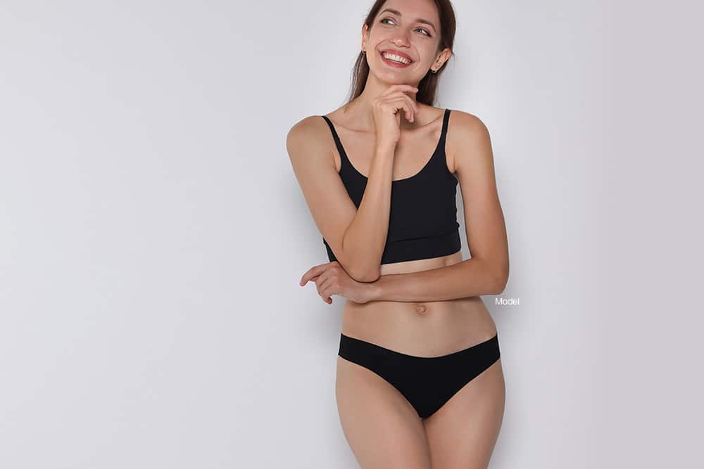 Woman in black underwear leaning against a gray wall